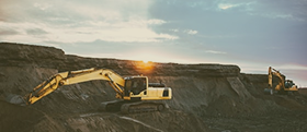 Yellow excavator on dirt mound with sunset glow